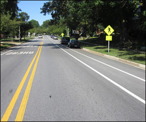 Two photographs show a two-lane street with a bike lane and a parking lane on the right, a shoulder on the left.  A post on the right has two signs -- on top is a yellow diamond-shaped sign showing a sillouette of a pedestrian walking, and below that is a rectangular sign saying 'DEAF-BLIND PEDESTRIANS.'  About 150 ahead of that we can see another yellow sign at a crosswalk.